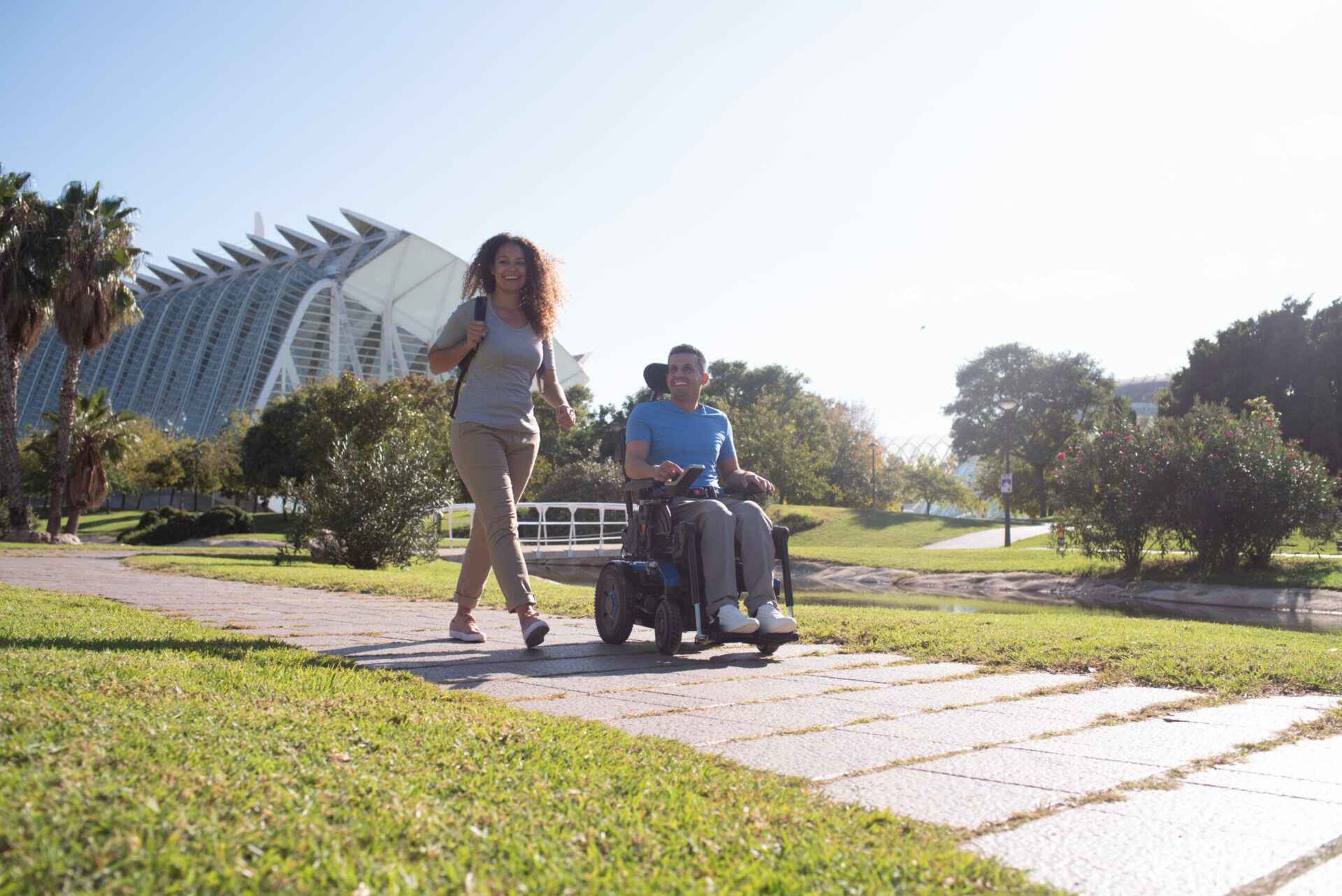 Powerchair-in-park-scaled-e1645103096606_compressed person walking next to another person who is in an electric wheelchair