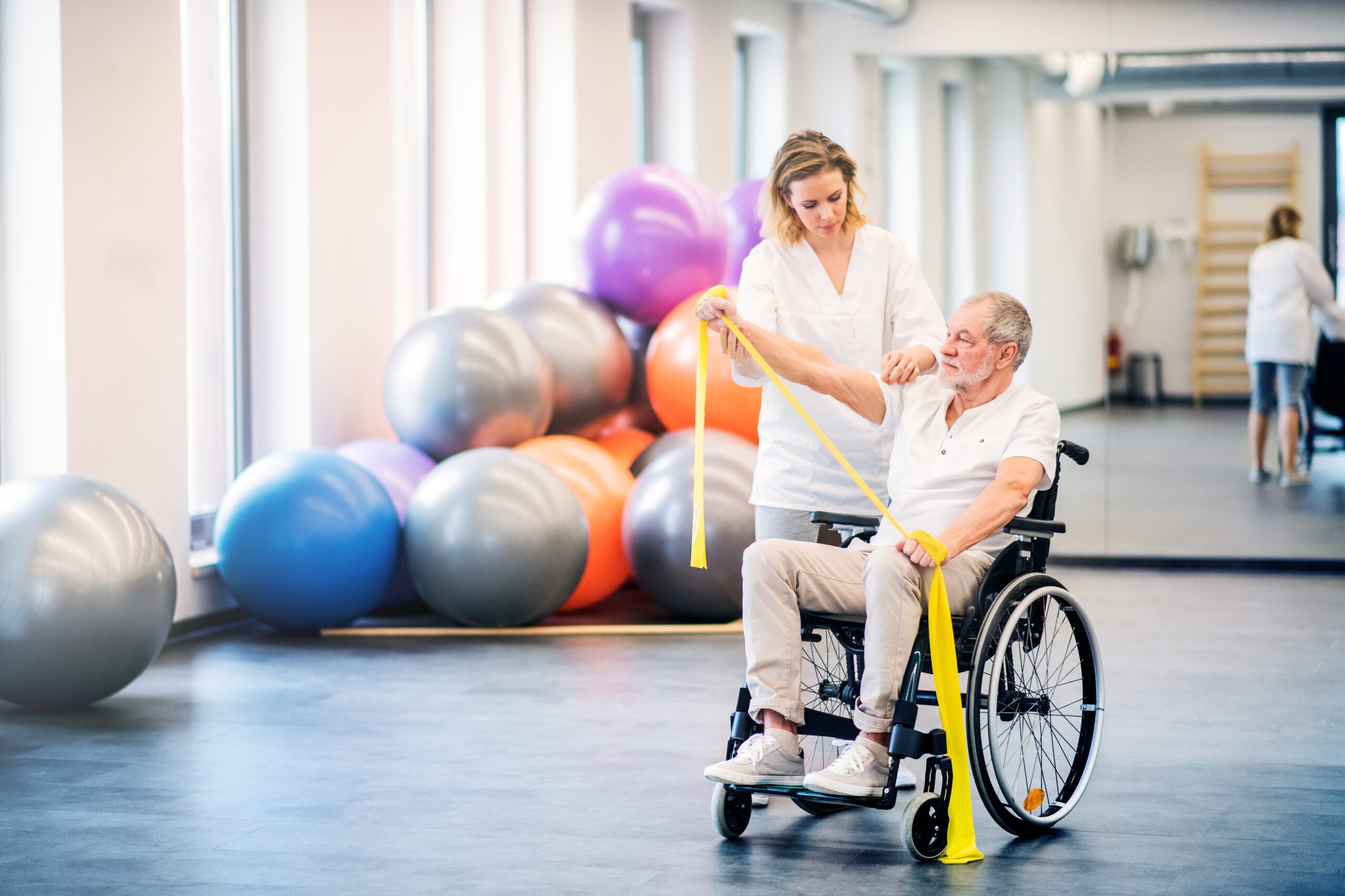 Young woman physiotherapist working with a senior man in wheelchair. Young attractive woman physiotherapist working with a senior man in wheelchair.