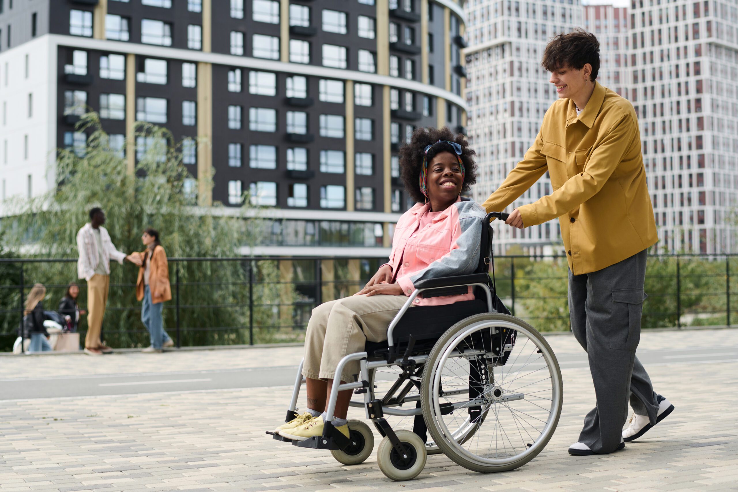 Multiethnic couple enjoying time outdoors Multiethnic couple enjoying time outdoors, young man riding his friend in wheelchair along the street