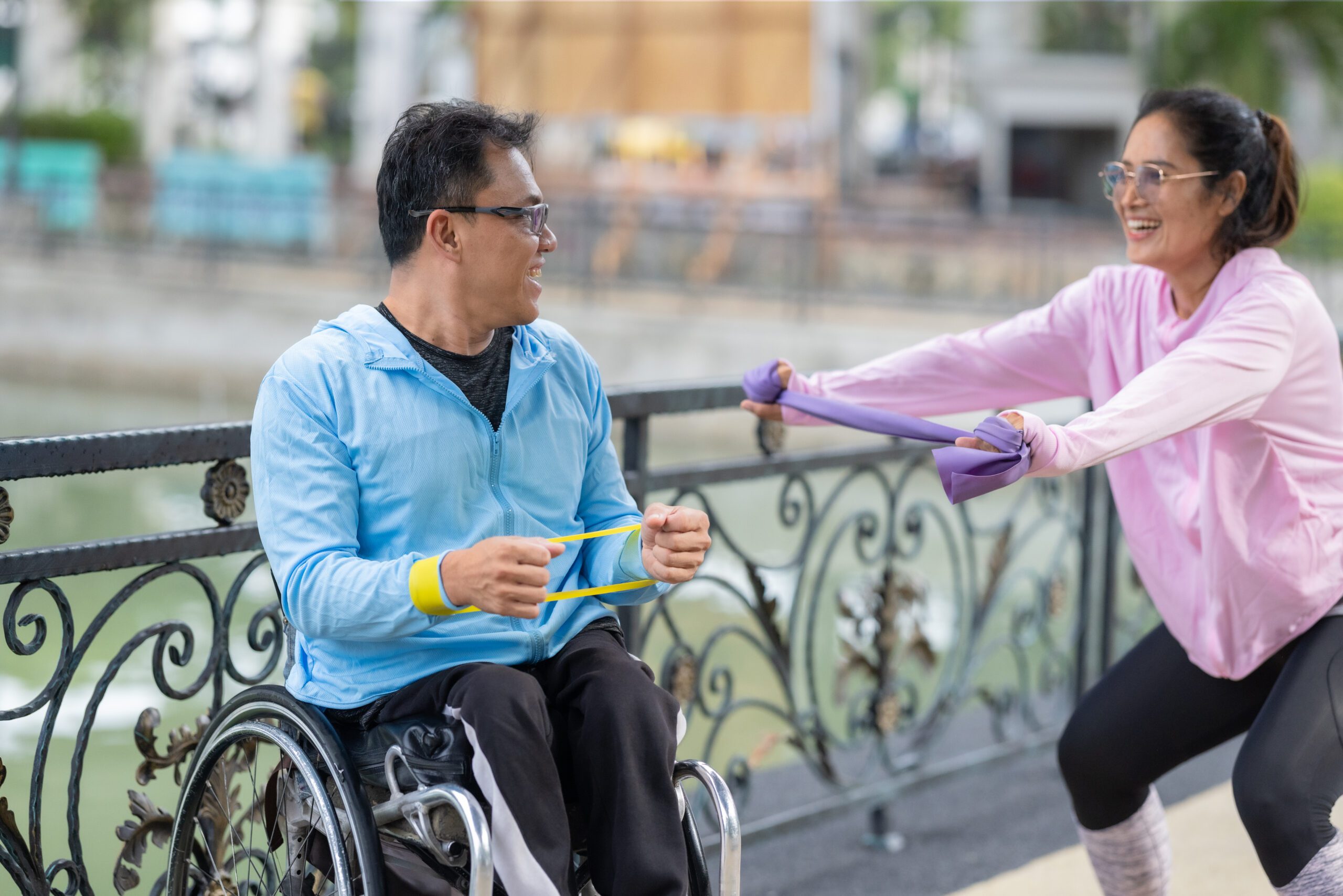 Wheelchair Fitness and Resistance Training with Partner A man in a wheelchair exercising, supported by his partner during a resistance, strengthening and cardio workout routine. This image highlights the themes of fitness, motivation, and perseverance.