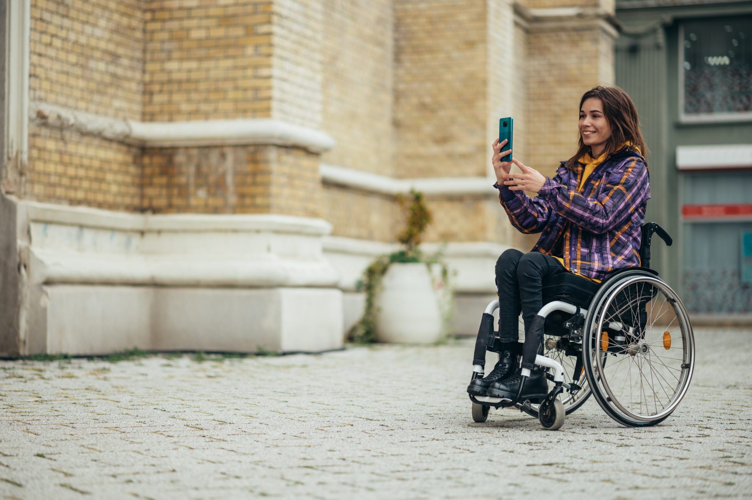 Young beautiful woman in wheelchair taking a selfie with her smartphone while out in the city