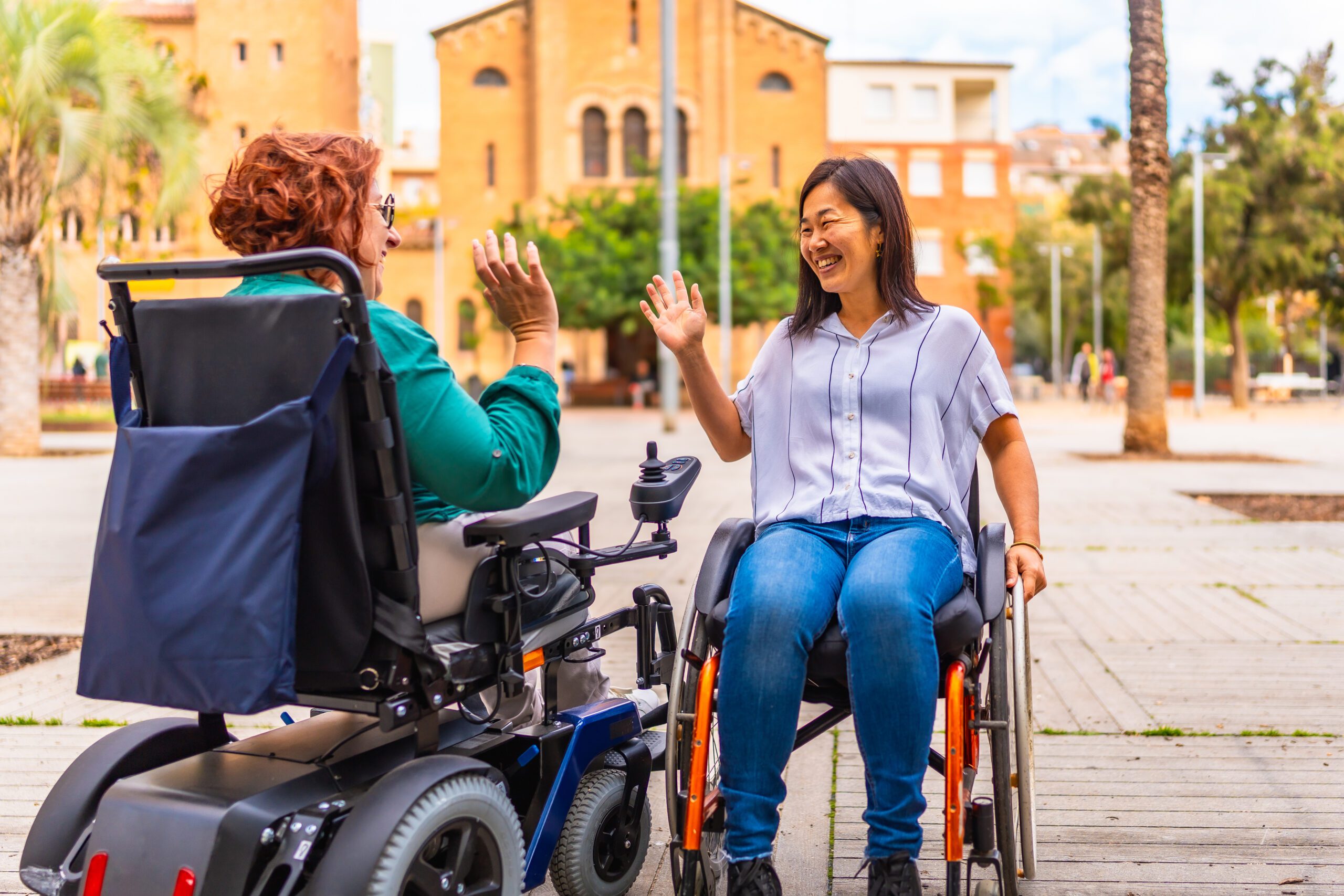 Women with disabilities in wheelchairs saying goodbye on the street Two multi-ethnic women with disabilities in wheelchairs saying goodbye on the street